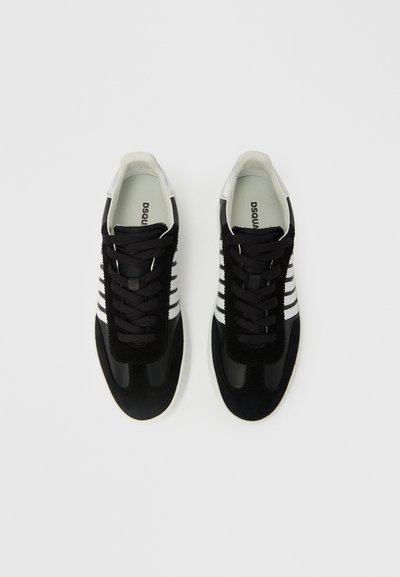 Baskets noires en daim et cuir. Caractéristiques des accents rayés blancs, une languette noire texturée et une semelle en caoutchouc blanche.