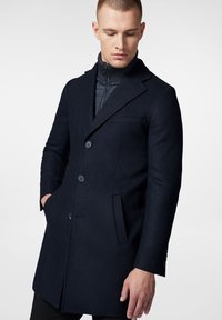 Granatowy wełniany p łaszcz o dopasowanym kroju, jednorzędowy, z wyłogami, dwoma guzikami i bocznymi kieszeniami. Gładka tekstura z minimalnymi detalami.