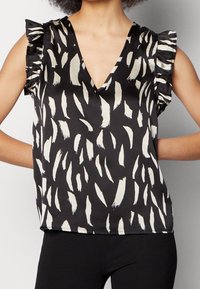 Haut sans manches noir avec un décolleté en V, présentant des motifs de coups de pinceau blancs et des accents volantés aux épaules. Tissu lisse et doux.