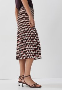 Gonna midi plissettata con motivo geometrico nei colori marrone, bianco e rosso. Presenta una vita aderente e una silhouette fluida.