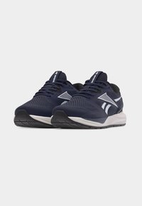 Ζ ευγάρι ναυτικό μπλε αθλητικά παπούτσια Reebok με λευκές λεπτομέρειες, μαύρες σόλες και κορδόνια σε λευκό φόντο.