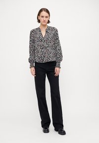 Svart blomstret bluse med v-hals, lange puffermer og elastiske mansjetter, med små rosa og hvite blomster. Brukt med svarte rette bukser.