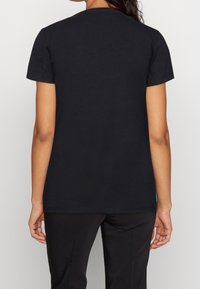 Camiseta de algodón negra con mangas cortas y cuello redondo. La parte posterior es lisa, con una textura suave y sin gráficos ni patrones visibles.