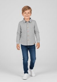 Szara koszula na długi rękaw z kołnierzykiem i brązowymi guzikami z przodu, w zestawieniu z niebieskimi dżinsami i białymi tenisówkami.