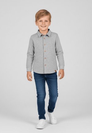 Szara koszula na długi rękaw z kołnierzykiem i brązowymi guzikami z przodu, w zestawieniu z niebieskimi dżinsami i białymi tenisówkami.