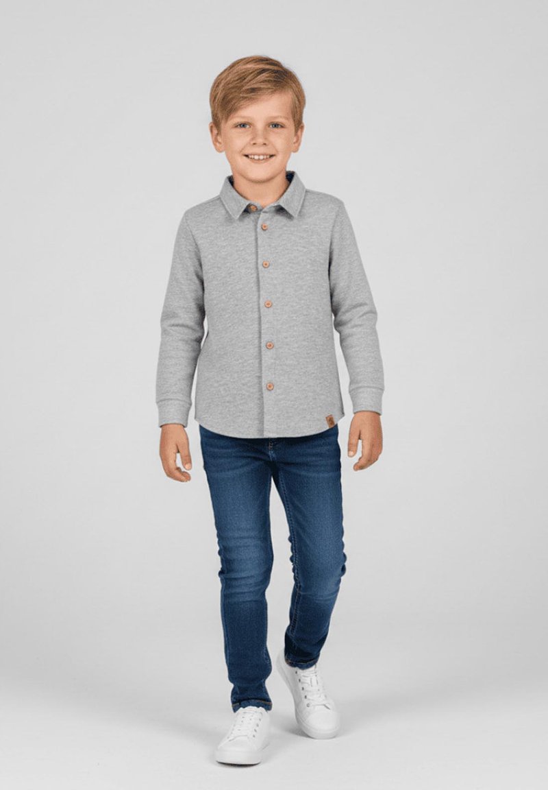 Szara koszula na długi rękaw z kołnierzykiem i brązowymi guzikami z przodu, w zestawieniu z niebieskimi dżinsami i białymi tenisówkami.