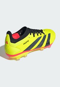 Crampon de football jaune vif avec des accents noirs, présentant une tige texturée, des lacets noirs et une semelle rose-rougeâtre avec des crampons transparents.