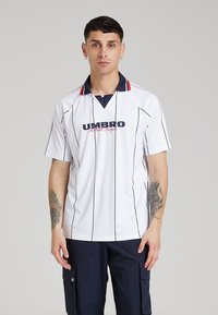 Polo shirt bianco a maniche corte con strisce verticali nere, logo ricamato "UMBRO Football League" in blu navy e colletto blu navy con dettagli rossi.