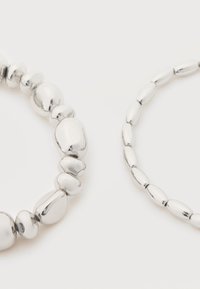 Deux bracelets en argent sur une surface blanche, l'un avec des perles arrondies irrégulières et l'autre avec des perles ovales uniformes.