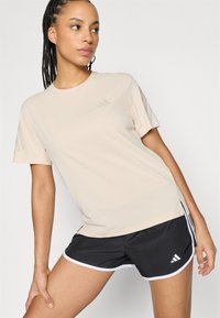 Lichtbeige sportief T-shirt met korte mouwen en een subtiel drie-strepen logo. Gecombineerd met zwarte shorts met witte biezen en logodetail.