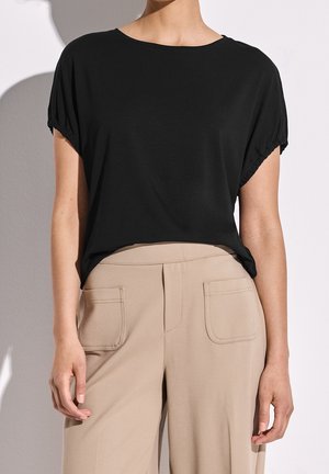 Top negro de manga corta hecho de tela suave con un corte relajado. Combinado con pantalones beige de tiro alto que cuentan con dos bolsillos delanteros.