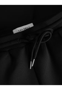 Shorts noirs avec une taille à cordon de serrage en corde noire, embouts en argent et une étiquette "LES DEUX" cousue dans la ceinture.