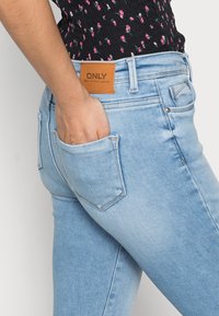 Jean en denim bleu clair avec une coupe slim, dotés de poches latérales et d'une étiquette en cuir marron à l'arrière de la taille avec "ONLY" embossé.