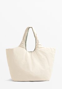 Sac fourre-tout beige clair en matériau matelassé, présentant une grande ouverture ovale et une texture lisse. Design minimaliste sans matériel visible.