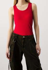 Débardeur rouge côtelé à larges bretelles, associé à un pantalon cargo noir avec des poches latérales et des détails en boucle. Silhouette ajustée.