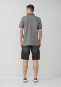 Grau Poloshirt mit schwarzem Kragen, kombiniert mit dunklen Denimshorts und weißen Sneakers. Der Schnitt ist lässig und präsentiert ein sauberes Design.
