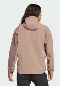 Veste à capuche de couleur marron clair avec une texture lisse. Dotée de poignets élastiques et d'une coupe décontractée. La vue arrière révèle une couleur contrastante sur les manches.