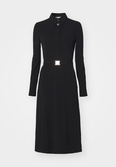 Black dress in soft fabric, featuring long sleeves, a collar, and a waist belt with a metallic buckle; includes a chest pocket.