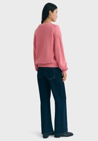 Pull en rose à côtes avec des manches ballon, associé à un jean évasé bleu foncé et des bottines noires. Design simple, tissu texturé.
