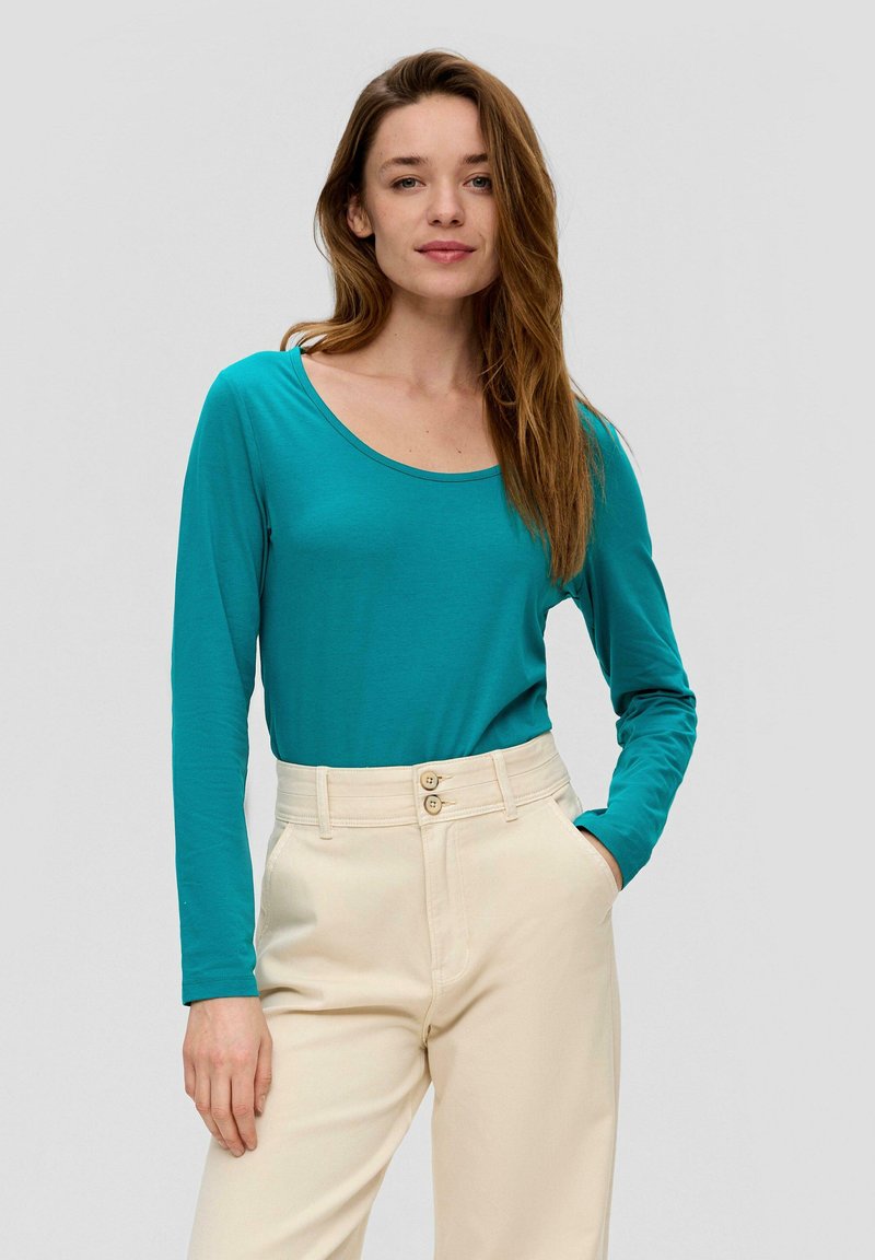 Teal lange mouwen top met een scoop halslijn, gecombineerd met hoog-waist beige broeken met een dubbele knopen sluiting en zijzakken.