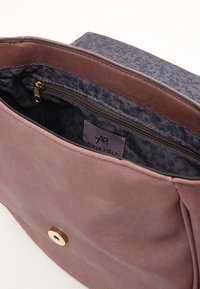 Różowa skórzana torba na ramię z złotym zapięciem. Wnętrze wykończone ciemnym kwiatowym podszewką i suwakiem. Widoczna metka marki.