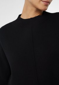 Czarny dzianinowy sweter z prążkowanym dekoltem, luźnym krojem i detalem szwu na środku. Gładka tekstura bez dodatkowych ozdób.
