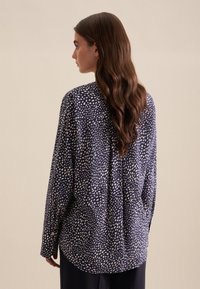 Camicia a maniche lunghe in navy con punti bianchi distribuiti, realizzata in tessuto morbido. Presenta una vestibilità comoda e un dettaglio di piega sul retro.