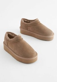 Chaussures slip-on en suède marron avec profile bas, intérieur rembourré et semelle extérieure en caoutchouc épaisse dotée d'un motif texturé.