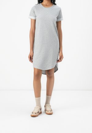 Woman wearing a light grey short-sleeve dress with rolled cuffs, beige socks, and beige sneakers with a brown leopard pattern.