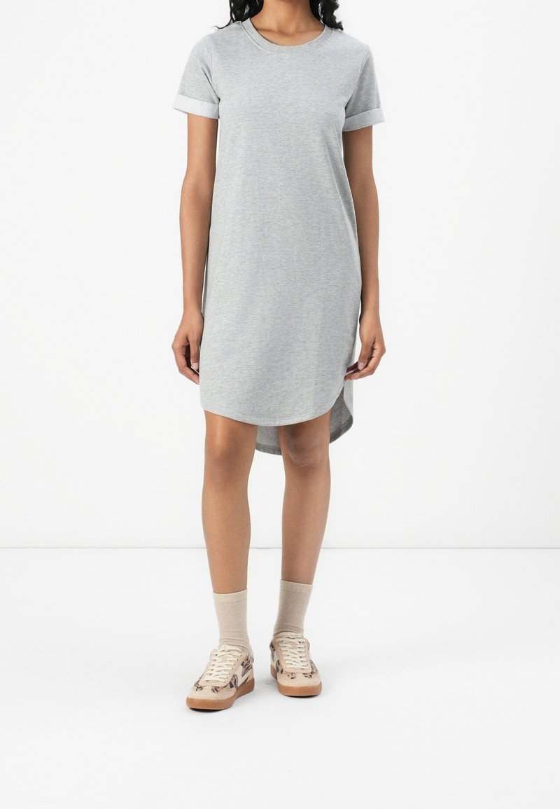 Femme portant une robe gris clair à manches courtes avec des revers roulés, des chaussettes beiges et des baskets beiges avec un motif léopard marron.