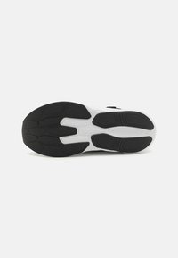 Semelle de chaussure de sport en noir et blanc présentant une surface en caoutchouc texturé avec des motifs variés pour l'adhérence et la flexibilité.