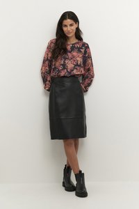 Blouse à manches longues à motifs floraux en bleu marine, majoritairement rose ; associée à une jupe crayon en cuir noir ; bottines à talons épais noires.