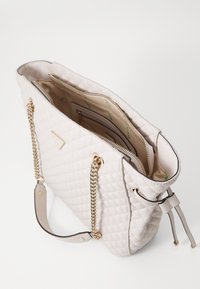 Quiltet beige håndtaske med guldkæde detaljer, dobbelte håndtag, lynlåslommer og et mønstret indvendigt foer. Tekstureret syntetisk materiale.