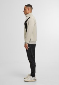 Beige mikina s vysokým límcem, černé boční akcenty; v kombinaci s černými kalhotami s jemnou texturou a bílým prošíváním. Krémové tenisky.