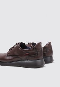 Zapatos de cuero marrón con un acabado suave, puntera redonda y suelas negras. Presentan costuras mínimas, diseño de cordones y una marca en el costado.