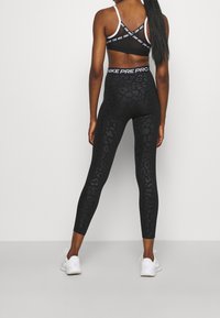 Czarne legginsy Nike z subtelnym wzorem w panterkę i wysokim stanem. W połączeniu z czarnym stanikiem sportowym z białymi ramiączkami.