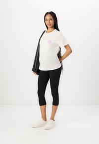 Hvit t-skjorte med rosa grafikk, kombinert med svarte croppede leggings. Modellen har på seg hvite sneakers og bærer en svart skulderveske.