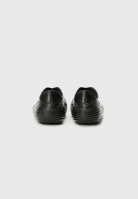 Fekete slip-on cipők hullámos textúrával, rugalmas anyagból készült. Lekerekített orral és puha szélekkel rendelkezik. Gumi talp a tapadásért.