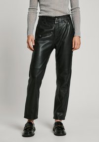 Black leather pants with a straight cut, featuring front pockets and a smooth texture, worn with shiny black loafers.