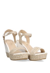 Sandalias de cuña en beige con tiras de tejido trenzado, diseño de punta abierta y un tacón de cuña blanco. Detalles de yute texturizado en la suela.