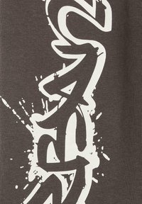 Szara koszulka z wyraźnym białym tekstem graficznym z detalami splatter, wykonana z miękkiej bawełnianej tkaniny o gładkiej fakturze.