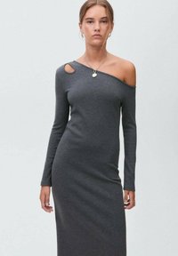 Abito lungo grigio a costine con design off-shoulder e dettagli cutout. Silhouette aderente, texture morbida e lunghezza fino al pavimento.