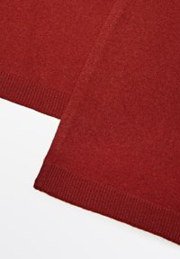 Tissu en maille rouge avec une texture douce, arborant un ourlet côtelé et une finition lisse dans l'ensemble. La forme est rectangulaire, mettant en évidence des détails de couture.