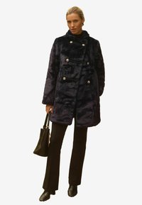 Jūras spēku tumši zila mākslīgās kažokādas mēteli ar dubultu aizdari, spīguļojošām sudraba pogām, augstu apkakli un sānu kabatām, saskaņota ar melnām biksēm un rokassomu.