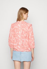 Blusa floral rosa com ombreiras franzidas, mangas longas bufantes e padrões florais brancos. Combinada com uma saia de jeans azul claro.