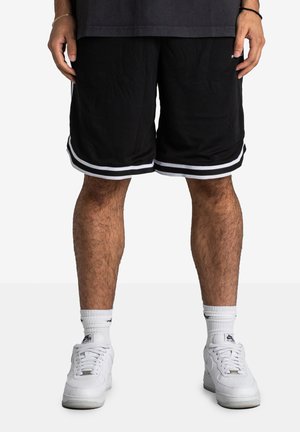 Shorts de sport noirs avec des rayures blanches sur les côtés, fabriqués en tissu respirant. Portés avec des baskets blanches et des chaussettes de sport blanches.