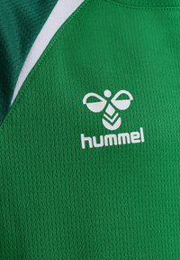 Zielona sportowa tkanina z białym logo marki Hummel przedstawiającym stylizowaną pszczołę oraz białym napisem na fakturowanym materiale.