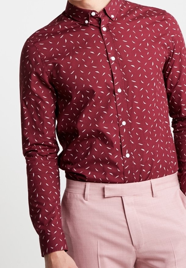 Camicia bordeaux con bottoni e motivi a foglia bianchi, maniche lunghe e colletto classico, abbinata a pantaloni su misura rosa chiaro.