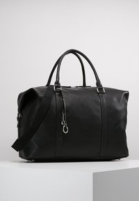 Sort faux læder duffel taske med buede håndtag og justerbar skulderrem, der har sølvfarvet hardware og en glat overflade.