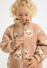 Fleece jacket in light brown with plush texture, featuring cream animal patterns, a high collar, and a front zipper.